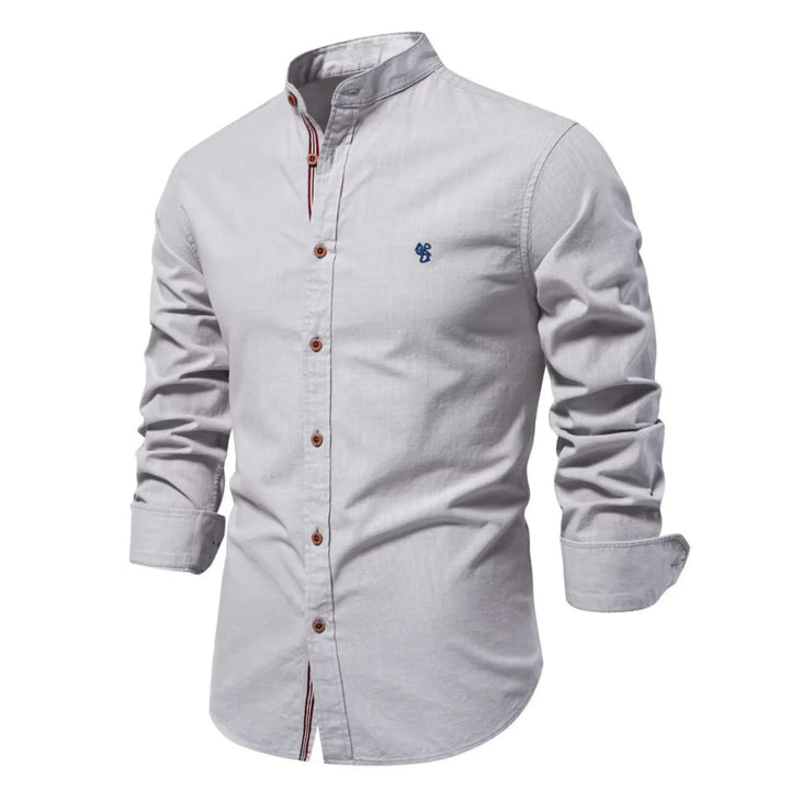 Cette chemise à manches longues de couleur grise claire présente un col Mao élégant, des boutons en bois contrastés et un petit logo brodé sur la poitrine. Parfaite pour un look à la fois chic et décontracté, elle est idéale pour les journées fraîches.