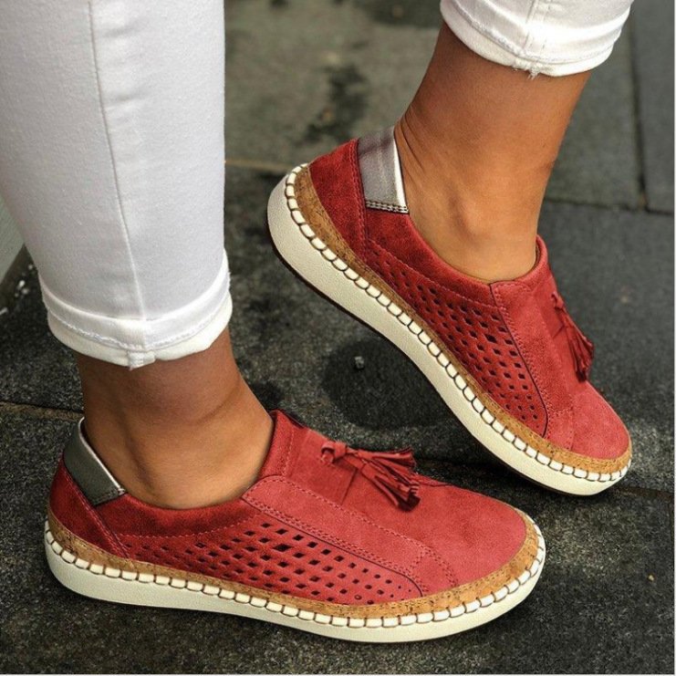 Pantoufles/mocassins plats rouges effet suédé, avec perforations latérales et pampilles, semelle beige avec liseré liège, portées en extérieur avec un pantalon blanc.