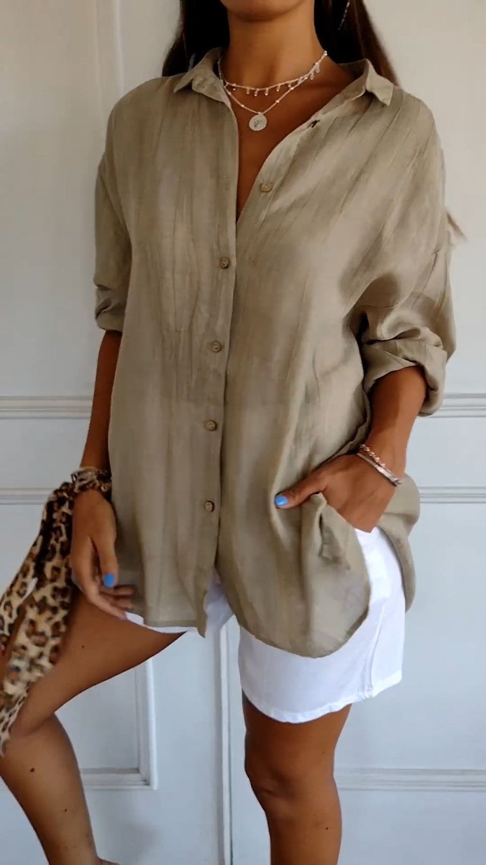 Chemise plissée pour femme beige, coupe ample avec col ouvert et manches retroussées, boutonnage devant, portée avec un short blanc.