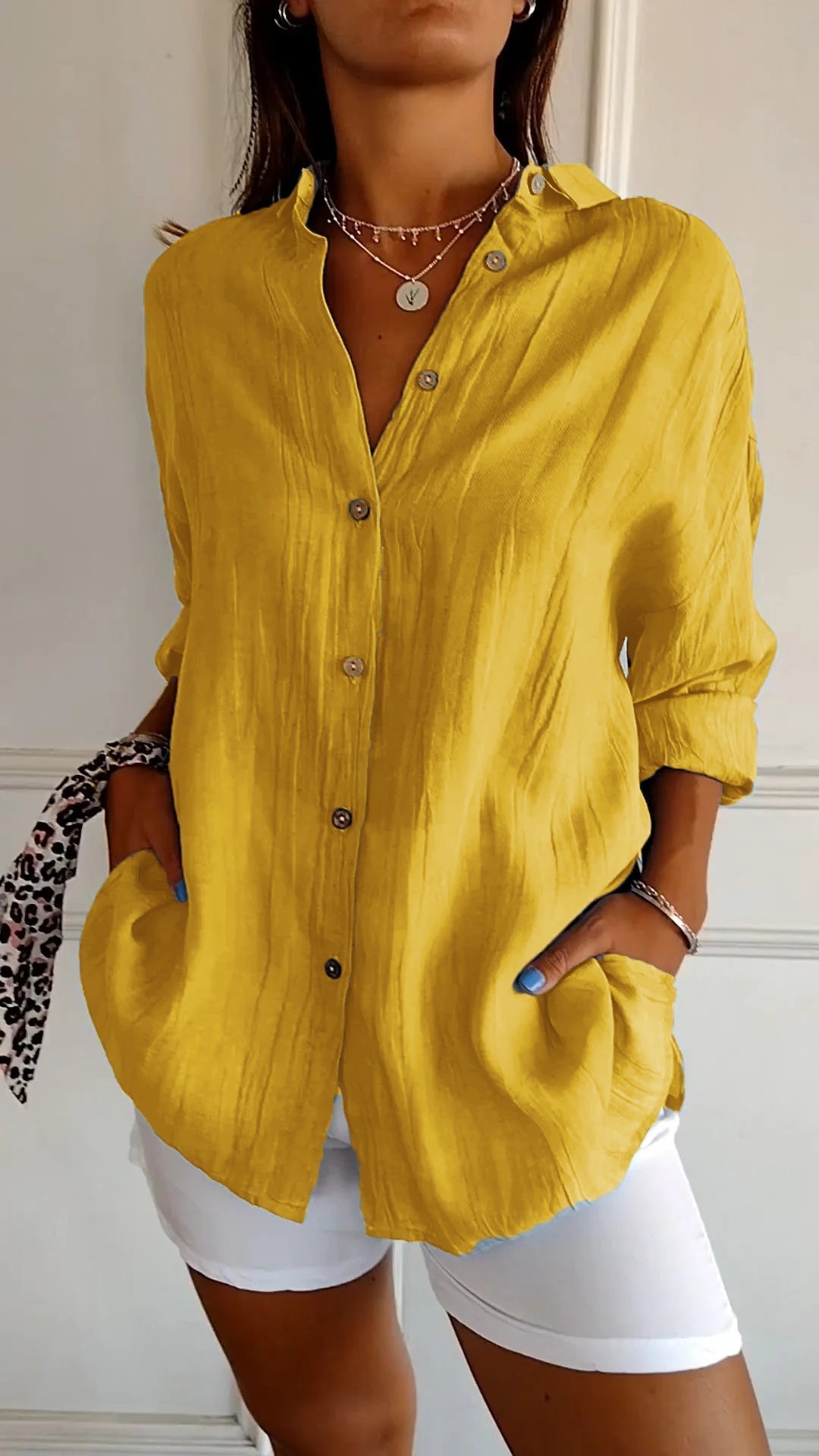 Chemise plissée pour femme jaune moutarde, coupe ample avec col ouvert et manches retroussées, boutonnage devant, portée avec un short blanc.