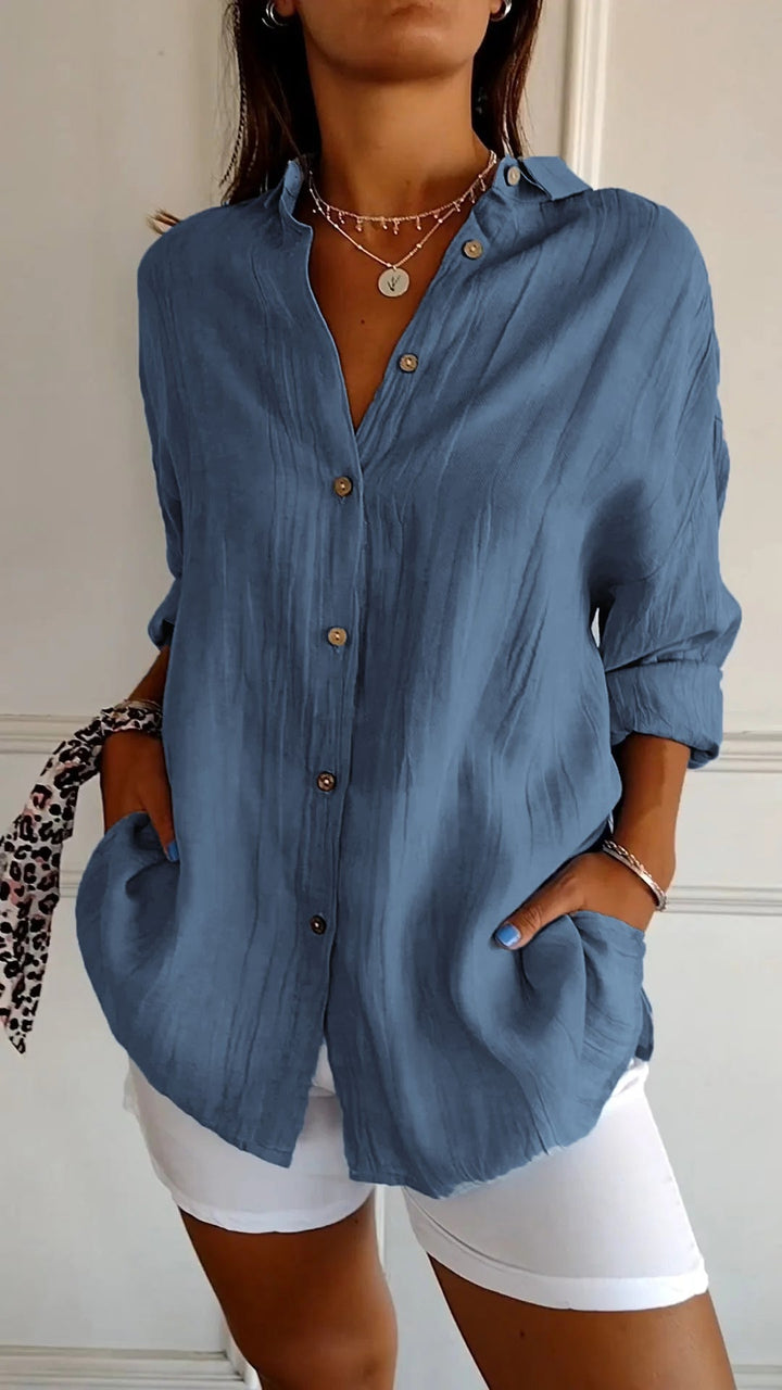 Chemise plissée pour femme bleu jean, coupe ample avec col ouvert et manches retroussées, boutonnage devant, portée avec un short blanc.