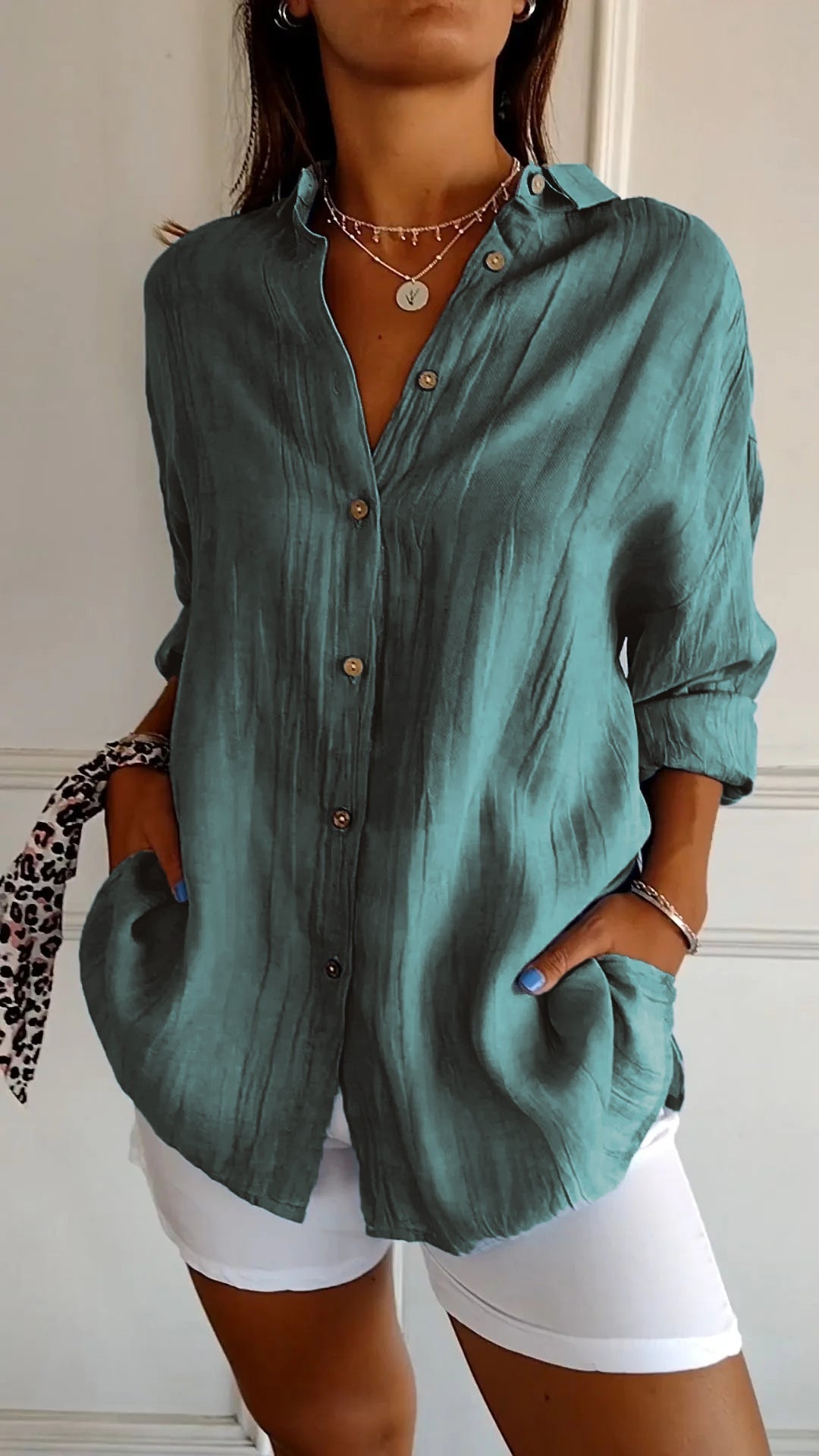 Chemise plissée pour femme vert canard, coupe ample avec col ouvert et manches retroussées, boutonnage devant, portée avec un short blanc.