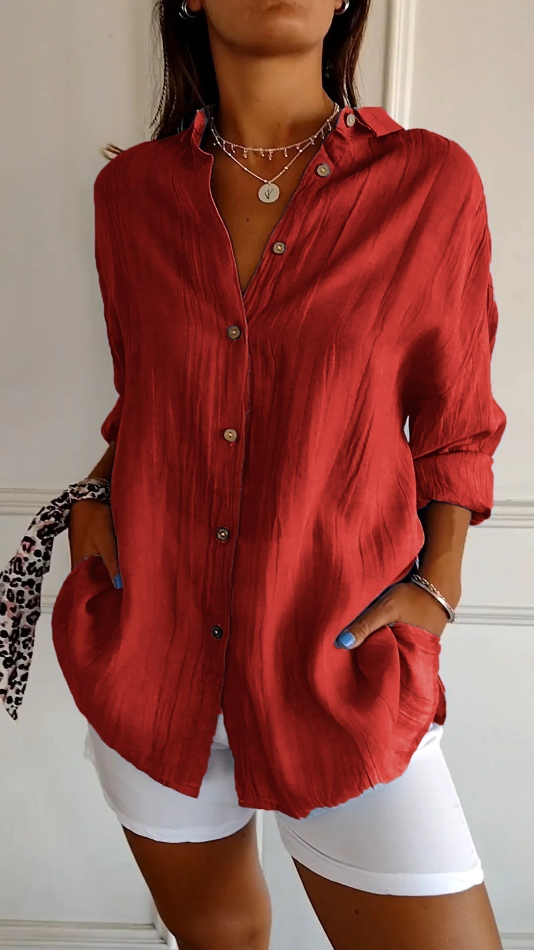 Chemise plissée pour femme rouge, coupe ample avec col ouvert et manches retroussées, boutonnage devant, portée avec un short blanc.