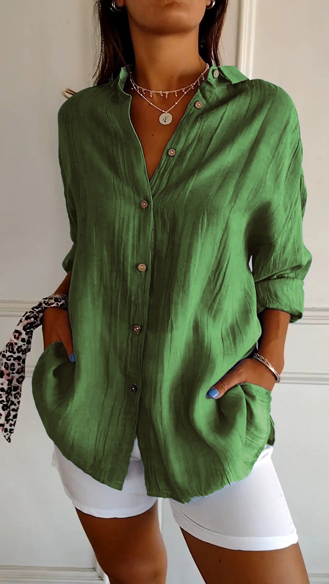 Chemise plissée pour femme verte, coupe ample avec col ouvert et manches retroussées, boutonnage devant, portée avec un short blanc.