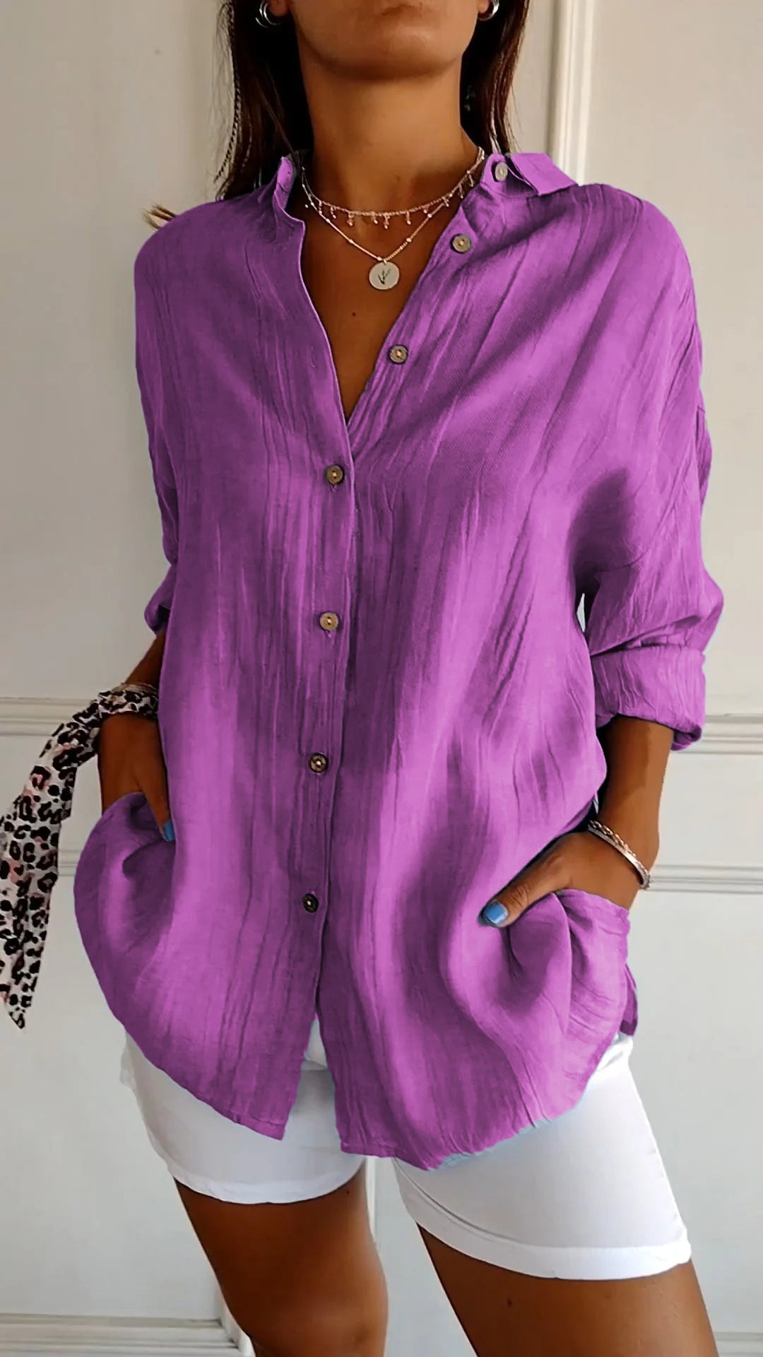 Chemise plissée pour femme violette, coupe ample avec col ouvert et manches retroussées, boutonnage devant, portée avec un short blanc.