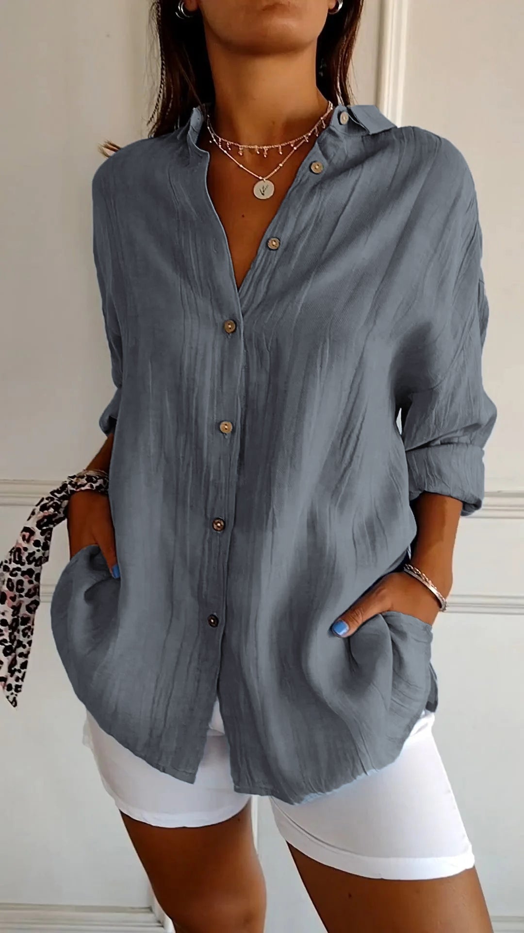 Chemise plissée pour femme gris bleu, coupe ample avec col ouvert et manches retroussées, boutonnage devant, portée avec un short blanc.