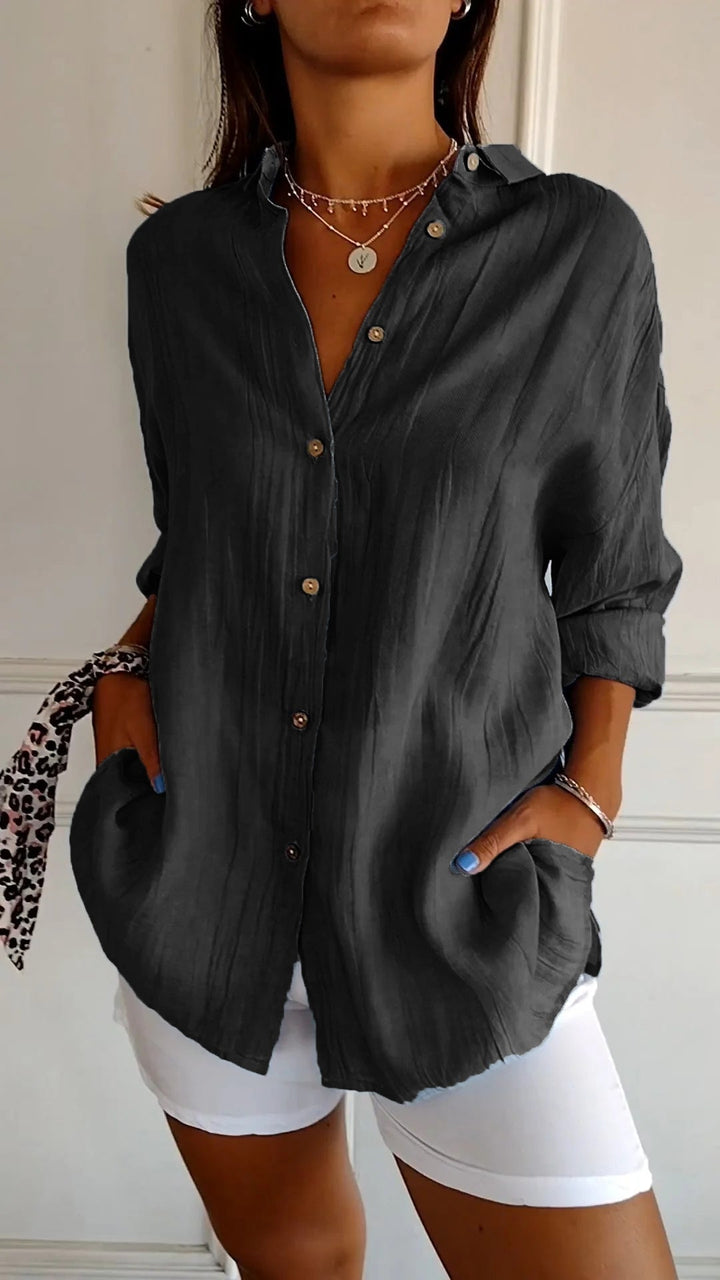 Chemise plissée pour femme noir foncé, coupe ample avec col ouvert et manches retroussées, boutonnage devant, portée avec un short blanc.
