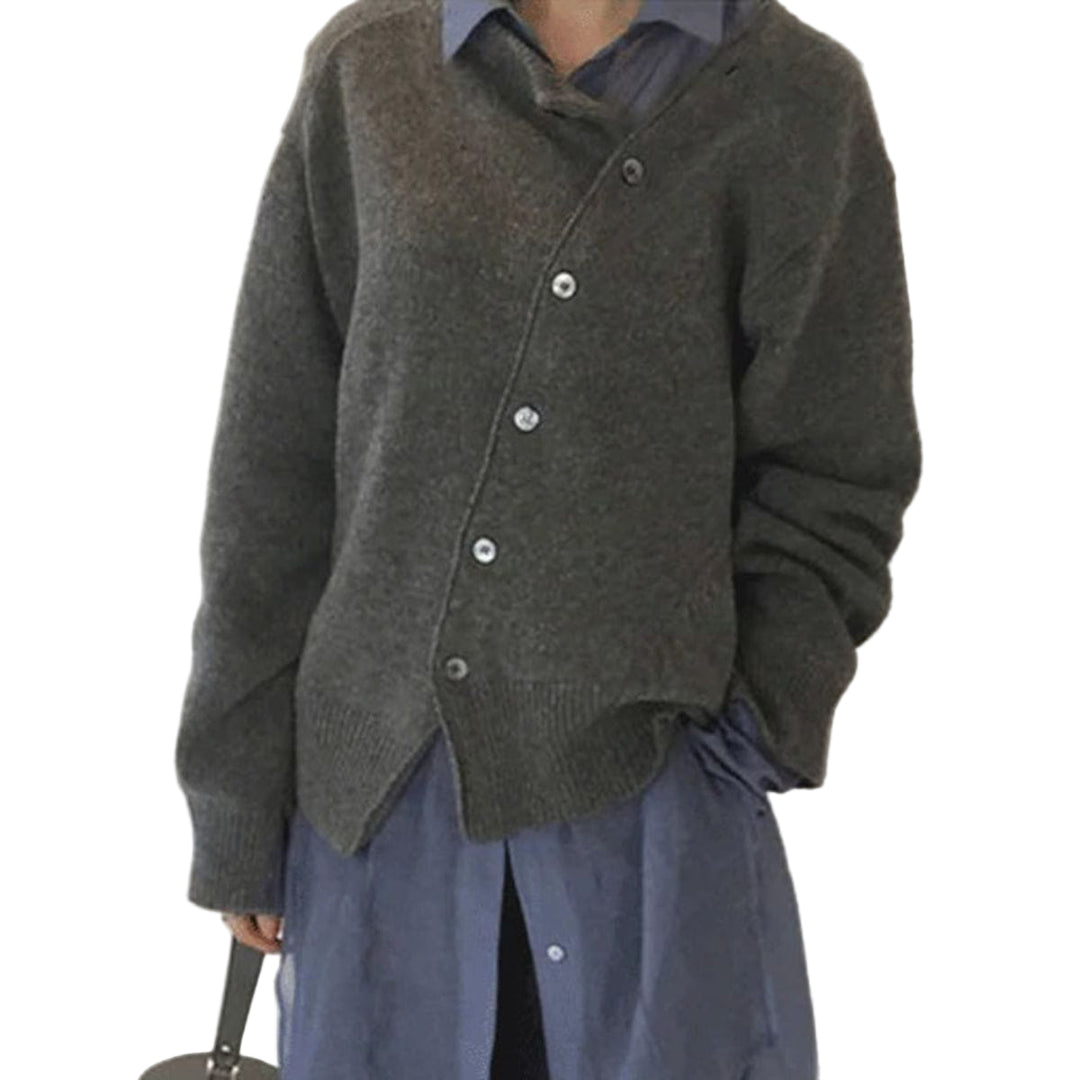 Femme portant un cardigan gris en maille avec des boutons gris et une coupe décontractée. Elle porte une chemise bleue en dessous, et le cardigan est superposé de manière élégante, créant un look moderne et confortable. Elle pose de profil, mettant en valeur son style élégant.