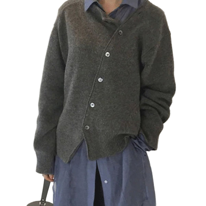 Femme portant un cardigan gris en maille avec des boutons gris et une coupe décontractée. Elle porte une chemise bleue en dessous, et le cardigan est superposé de manière élégante, créant un look moderne et confortable. Elle pose de profil, mettant en valeur son style élégant.