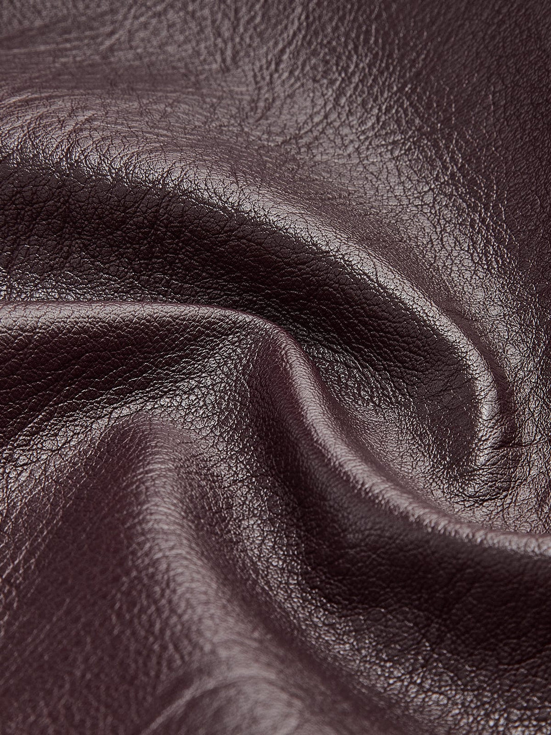 Gros plan sur le tissu en simili cuir bordeaux, mettant en valeur sa texture lisse et brillante, soulignant la qualité et l'élégance du matériau pour un look moderne.