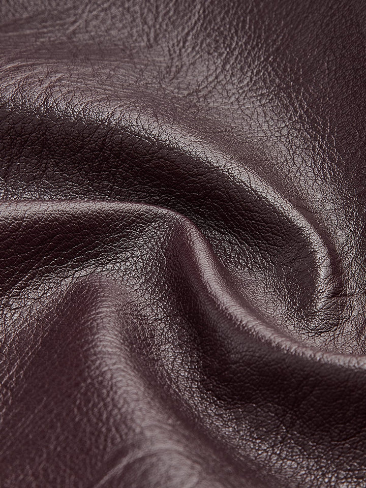Gros plan sur le tissu en simili cuir bordeaux, mettant en valeur sa texture lisse et brillante, soulignant la qualité et l'élégance du matériau pour un look moderne.