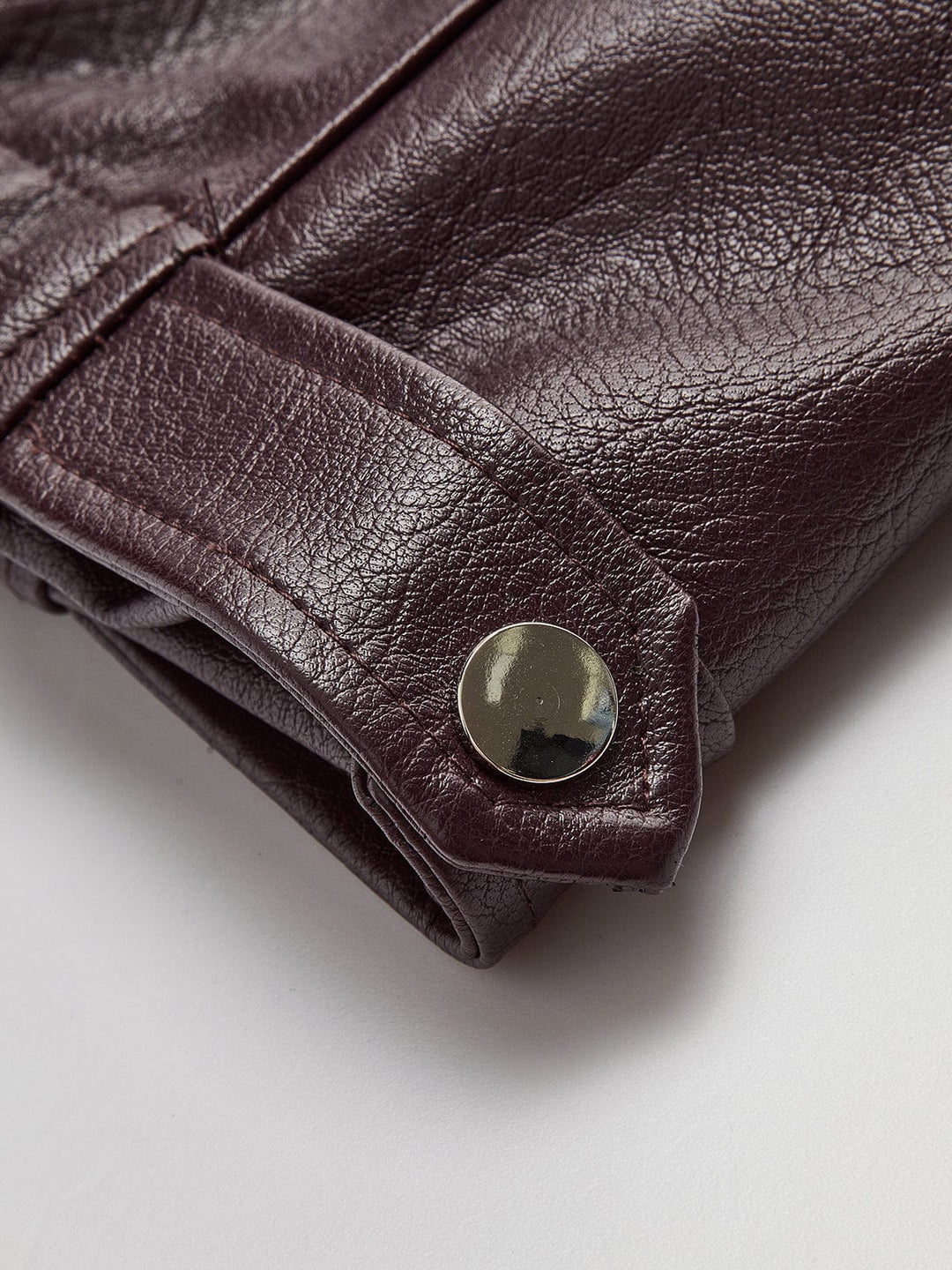 Gros plan sur le détail des manches avec bouton pression métallique, mettant en valeur la texture du simili cuir bordeaux et les finitions soignées de la veste.