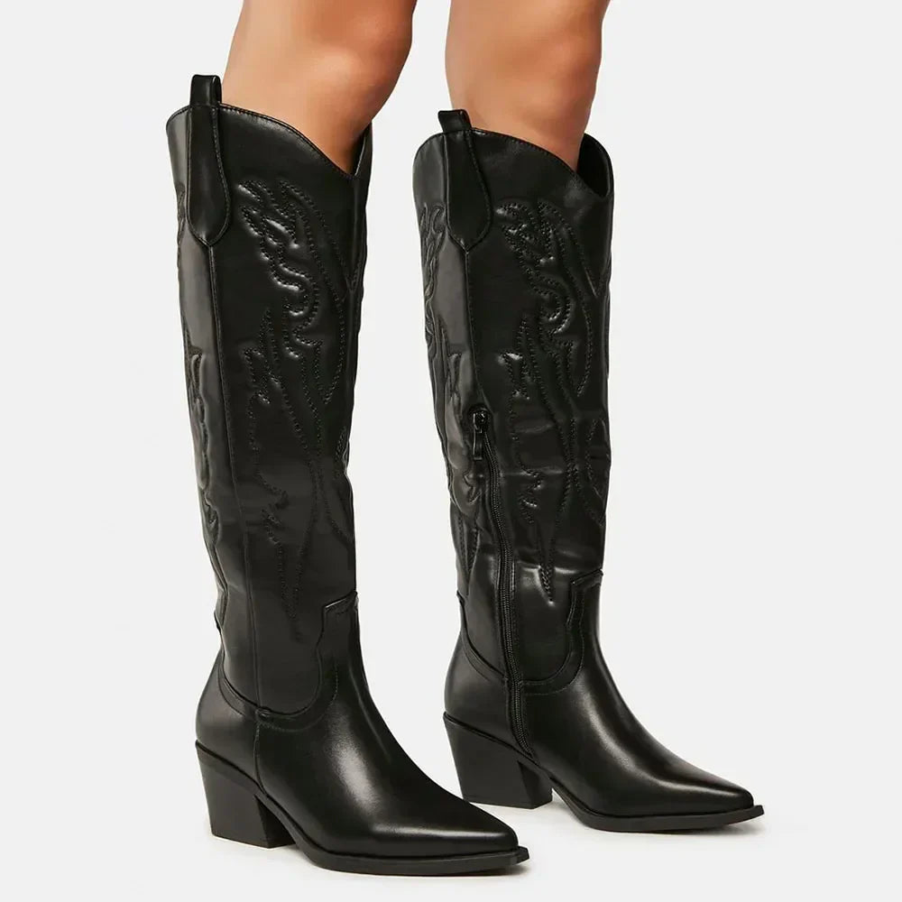 Bottes western noires à talons carrés pour femme, avec des coutures décoratives et un design épuré. Elles sont dotées d'une fermeture éclair sur le côté et présentent une forme pointue à l'avant, offrant un style à la fois moderne et audacieux.