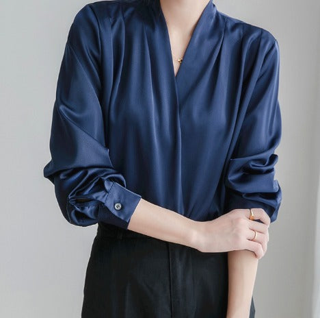 Blouse élégante à manches bouffantes et décolleté en V, portée par une femme avec un pantalon noir et un anneau.