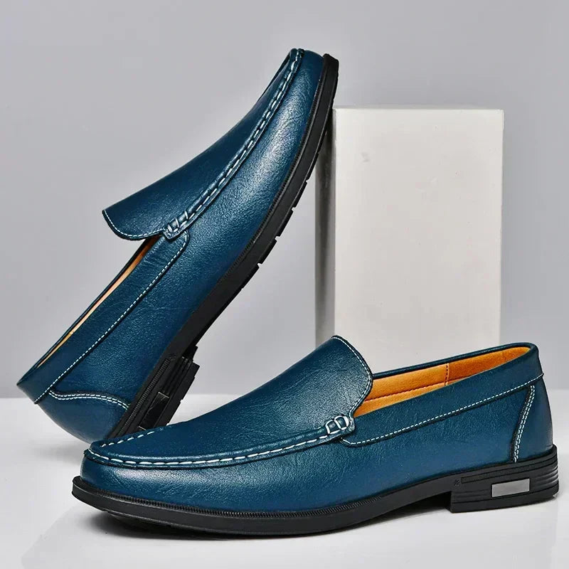 Mocassins classiques homme bleu marine en similicuir, coutures contrastées et semelle noire antidérapante, présentés sur socle  look moderne et raffiné.