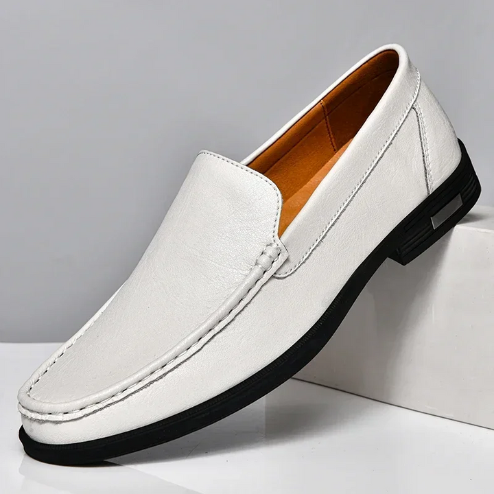 Mocassin classique homme blanc en similicuir, finition lisse avec coutures apparentes et semelle noire, présenté sur socle style moderne et élégant.