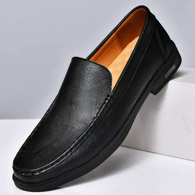 Mocassin classique homme noir en similicuir, finition lisse avec coutures apparentes et semelle noire, présenté sur socle  style moderne et élégant.