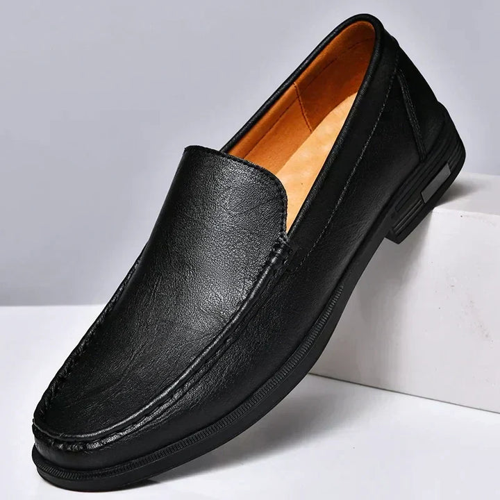 Mocassin classique homme noir en similicuir, finition lisse avec coutures apparentes et semelle noire, présenté sur socle  style moderne et élégant.