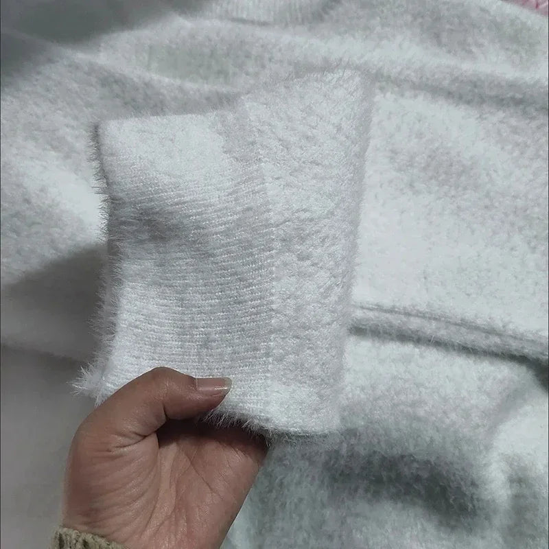 Gros plan d'une main ajustant les boutons en perle d'un cardigan blanc en tricot doux. Le tissu duveteux et les détails des boutons ressortent clairement sur l'image.