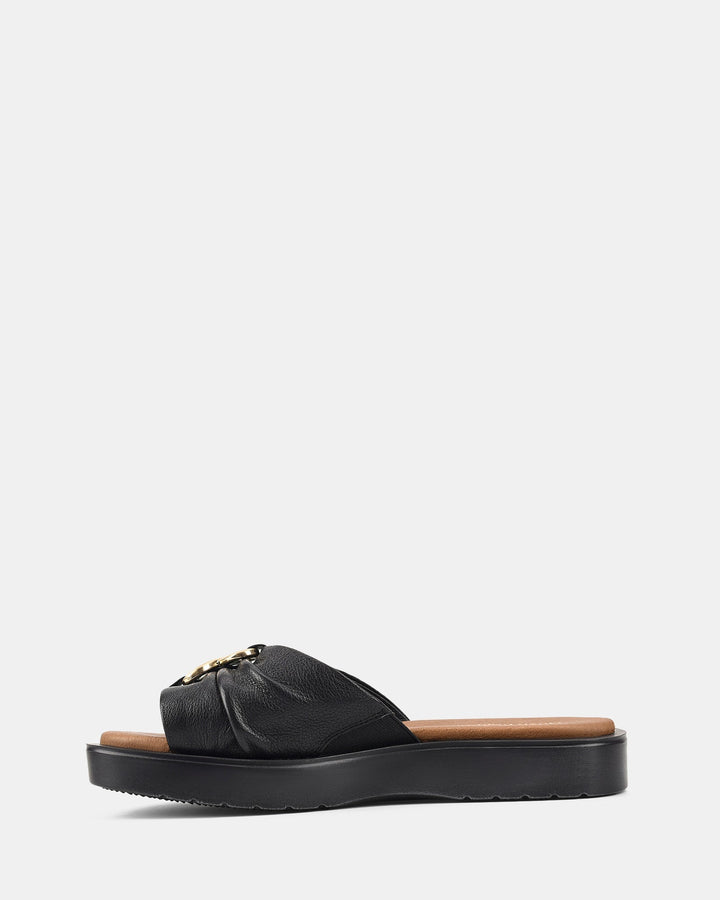 Sandales élégantes à lanière noire avec une boucle dorée distinctive, offrant une semelle ondulée pour un confort optimal et un style raffiné.