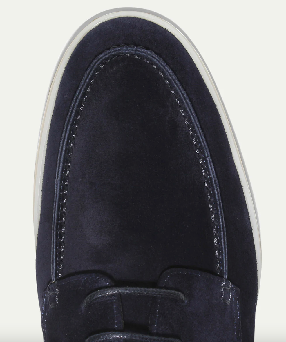 Gros plan sur l’avant d’un mocassin derby en suédine bleu marine, avec coutures apparentes et finitions soignées, semelle claire.