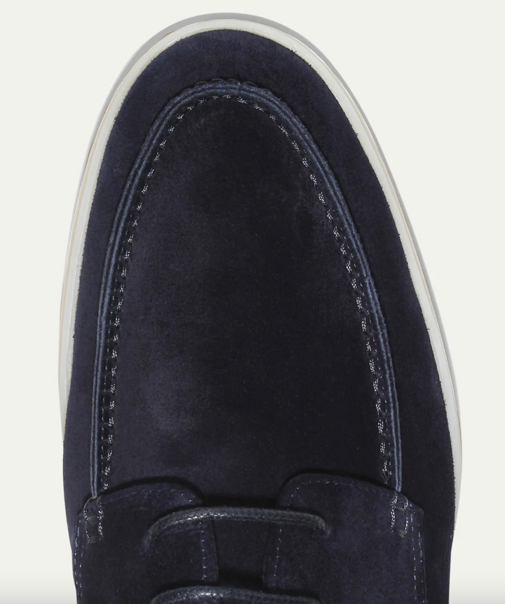 Gros plan sur l’avant d’un mocassin derby en suédine bleu marine, avec coutures apparentes et finitions soignées, semelle claire.