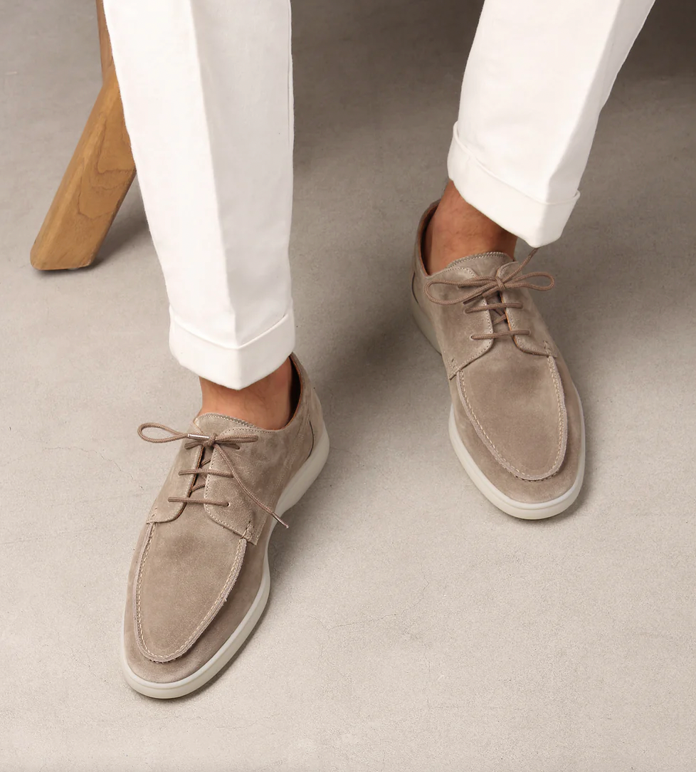 Mocassins derbies en suédine beige avec lacets et semelle claire, portés avec un pantalon blanc, style chic et décontracté.
