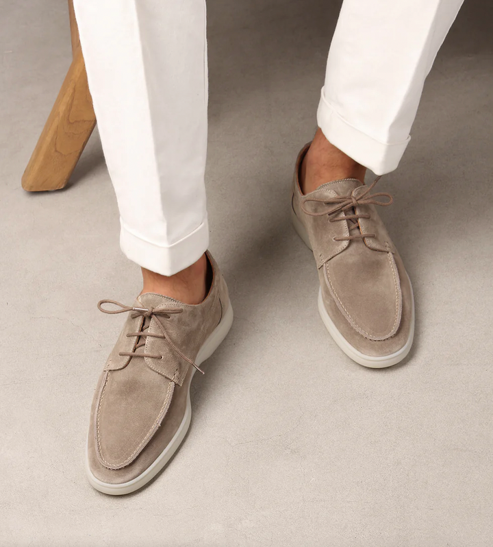Mocassins derbies en suédine beige avec lacets et semelle claire, portés avec un pantalon blanc, style chic et décontracté.