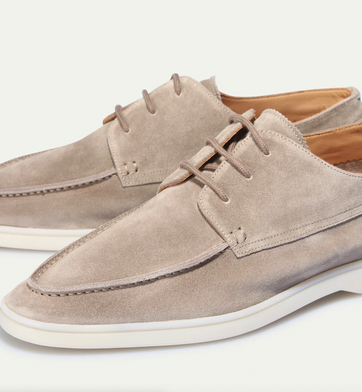 Gros plan sur une paire de mocassins derbies en suédine beige avec lacets, couture mocassin sur l’avant et semelle claire, style chic décontracté.