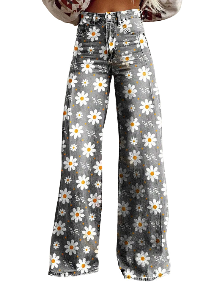 Jean ample pour femme Morwenna gris à imprimé marguerites blanches et jaunes, taille haute et jambes très larges, porté sur fond de mur en béton.