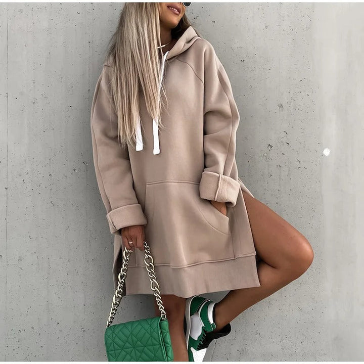 Sweat à capuche oversize beige porté en robe, cordons blancs et grande poche, manches longues avec fentes latérales, sac à chaîne.