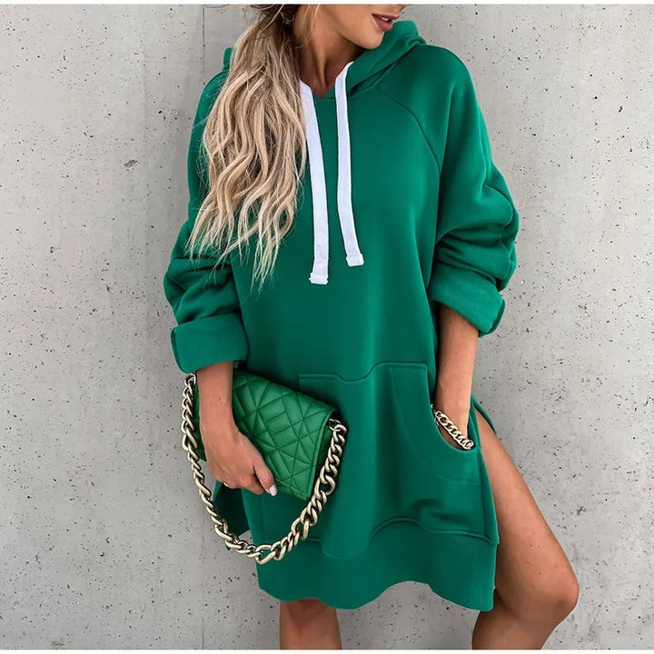 Sweat à capuche oversize vert avec cordons blancs et grande poche, fentes latérales, porté en robe avec pochette matelassée verte à chaîne.