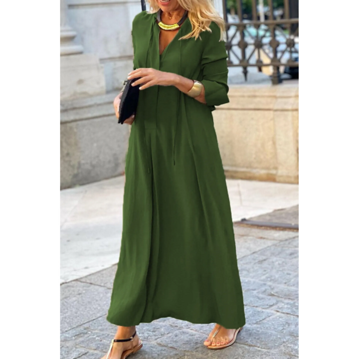 Femme portant la robe maxi d’été Nadège, longue robe vert olive fluide à manches 3/4 et col en V, coupe ample et élégante, portée avec des sandales et des accessoires dorés style moderne et chic en extérieur.
