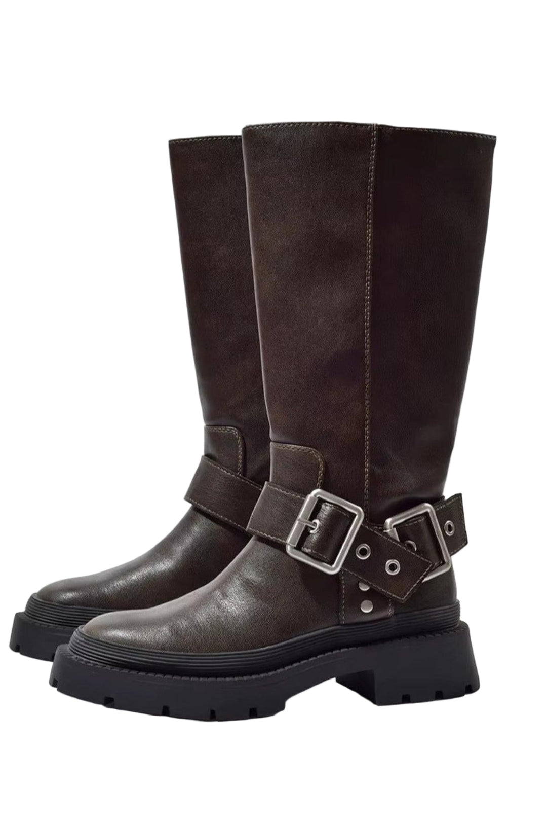 Bottes hautes pour femme en cuir synthétique marron à semelles crantées noires épaisses. Leur design est rehaussé d'une bride de cheville décorative avec une boucle en métal argenté, apportant une touche moderne et audacieuse. Les coutures apparentes et la texture mate du cuir soulignent un style tendance et robuste. Présentées de profil sur un fond clair, les bottes mettent en valeur leur élégance et leur solidité.
