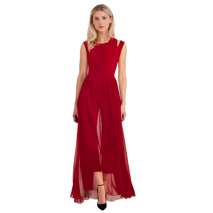 Robe longue et fluide pour femme, en rouge vif, avec un haut ajusté et une jupe ample qui tombe gracieusement jusqu'aux pieds. La robe présente des détails élégants au niveau des épaules et une coupe moderne. Elle est portée avec des chaussures noires à talons fins, créant un look chic et sophistiqué.