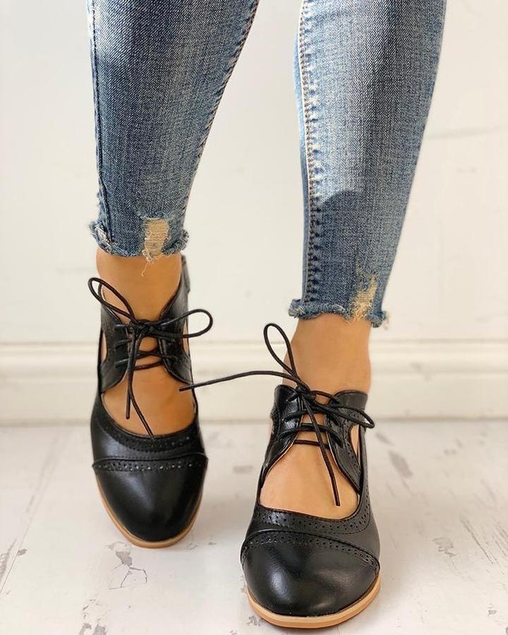 Chaussures noires rétro à lacets avec découpes et détails perforés, bout arrondi, portées avec un jean sur un sol clair, vue de face.