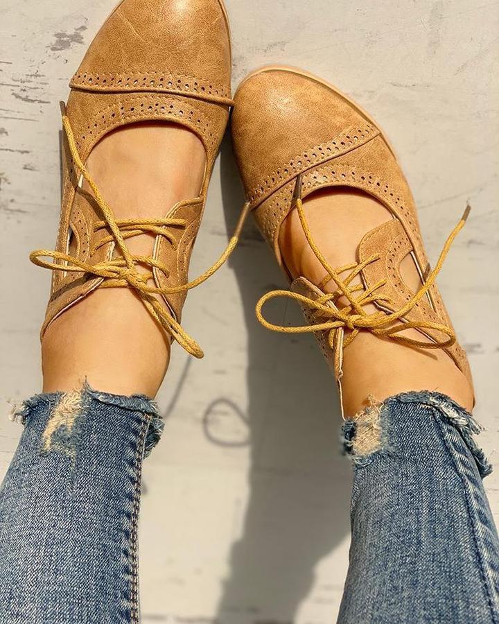 Vue du dessus de chaussures camel style rétro à lacets, bout arrondi et détails perforés, portées avec un jean sur sol clair.