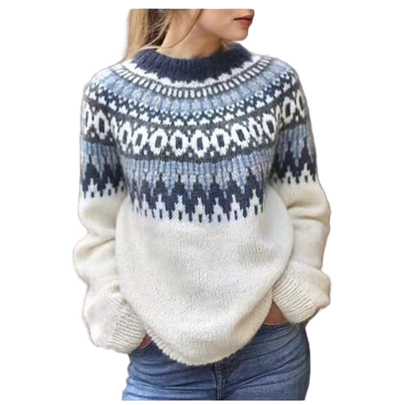 Femme portant un pull d’hiver en maille écru orné de motifs nordiques bleus et gris sur le haut, les mains dans les poches d’un jean, posant devant un fond en bois pour un style chaleureux et saisonnier.