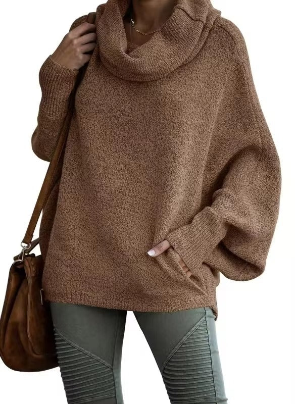 Femme portant un pull ample à manches chauve-souris de couleur marron chaud avec un grand col drapé. Le tissu épais et texturé apporte une sensation de douceur et de confort. Elle associe ce haut à un pantalon kaki ajusté et un sac en cuir marron, créant un look hivernal casual et élégant.