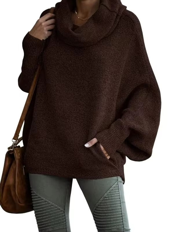 Femme vêtue d’un pull ample à manches chauve-souris de couleur marron foncé avec un large col drapé. Le tissu épais et doux évoque confort et chaleur, idéal pour l’hiver. Elle complète sa tenue avec un pantalon kaki texturé et un sac en cuir marron, créant un style chic et décontracté.