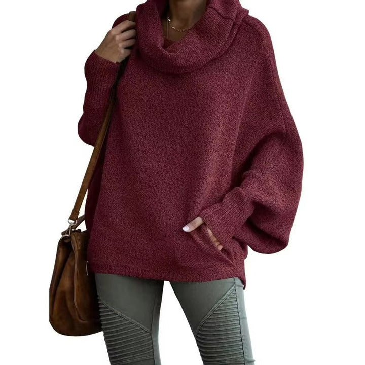 Femme portant un pull ample à manches chauve-souris de couleur Bordeaux avec un large col drapé. Le tissu en maille douce et épaisse évoque confort et chaleur. Elle complète sa tenue avec un pantalon kaki texturé et un sac en cuir marron, pour un look d’hiver à la fois chic et décontracté.