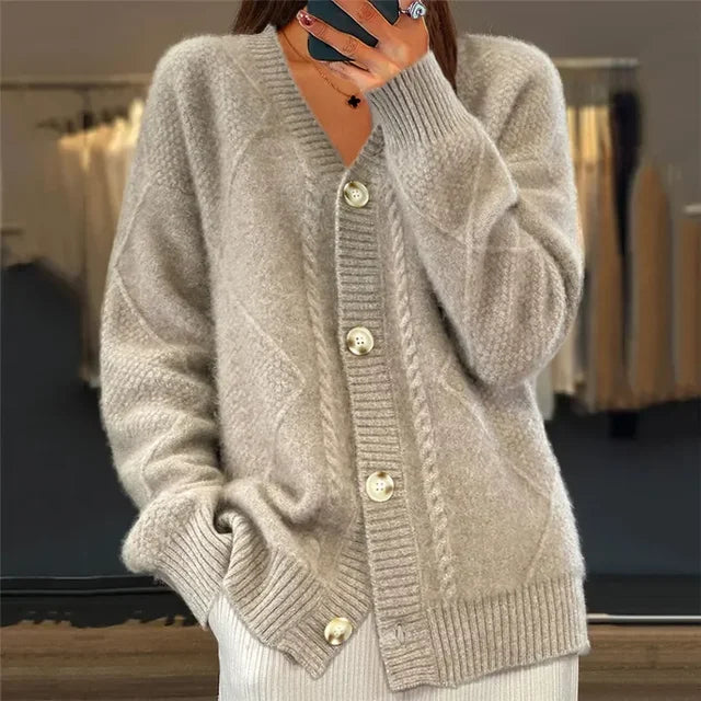 Femme portant un cardigan beige en tricot avec un col en V, des boutons blancs et un motif torsadé. Elle garde une main dans la poche, dégageant une allure chic et confortable.