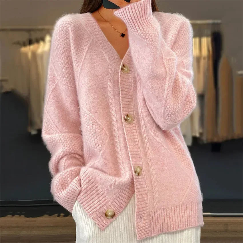Femme portant un cardigan rose pâle en tricot avec un col en V, des boutons en bois et un motif torsadé. Elle garde une main dans la poche, affichant un look décontracté et élégant.