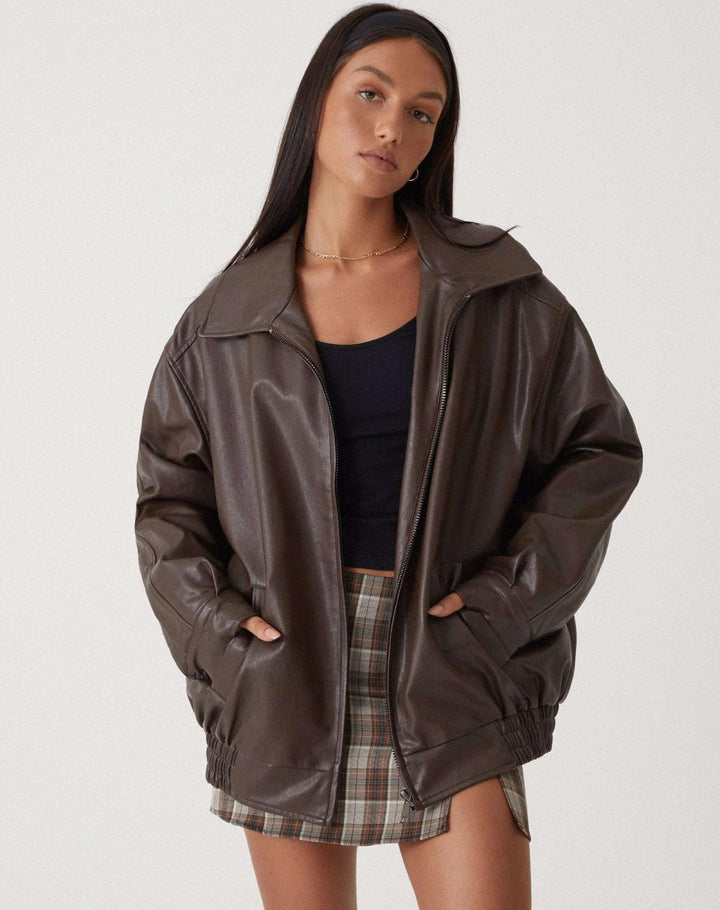 Veste oversize en PU pour femme, modèle Ombeline. Veste en simili-cuir marron à la coupe ample, portée avec une jupe à carreaux et un t-shirt noir. Un look décontracté et moderne, parfait pour l'hiver.