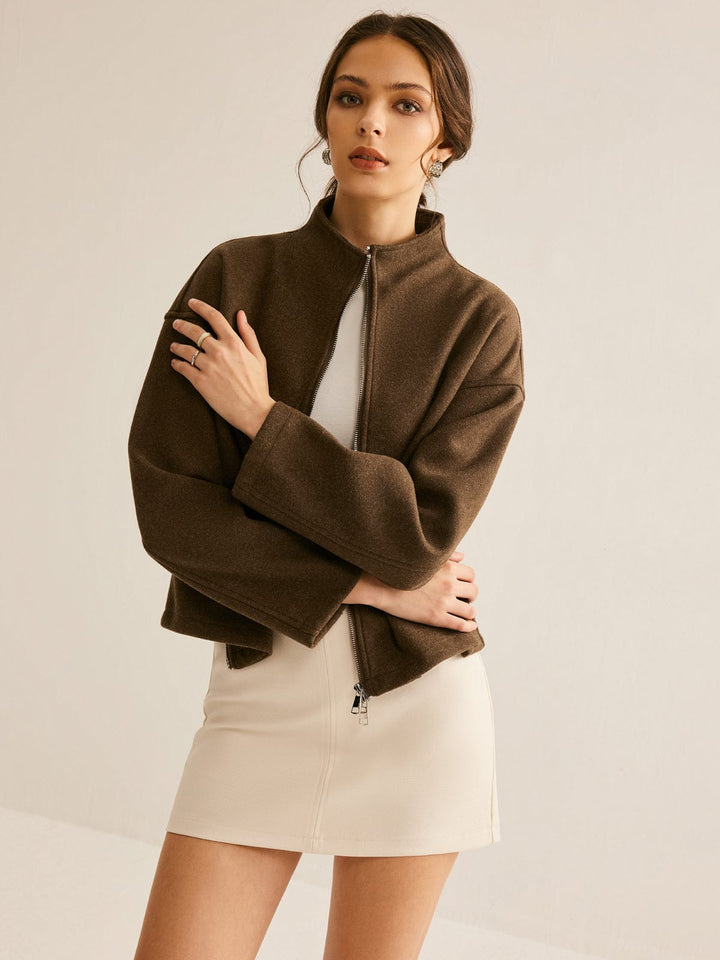 Femme portant un manteau court marron à col montant et fermeture zippée, associé à une robe courte beige, pour un look à la fois élégant et contemporain.