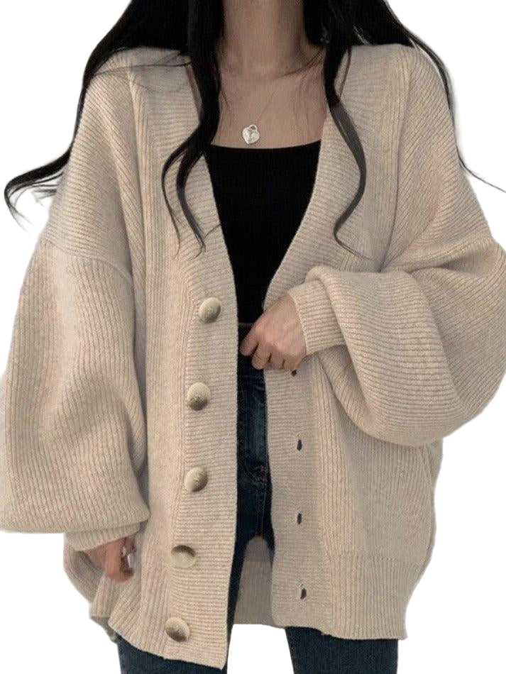 Femme portant un cardigan long en maille beige clair avec de grands boutons, coupe oversize et manches amples. Elle le combine avec un haut noir et un jean foncé pour un style moderne, décontracté et chaleureux idéal pour l’automne ou l’hiver.
