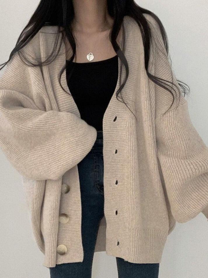 Femme portant un cardigan oversize en maille beige avec de grands boutons apparents sur le devant. Elle l’associe à un débardeur noir et un jean bleu ajusté pour un style moderne, confortable et élégant, parfait pour les journées fraîches.