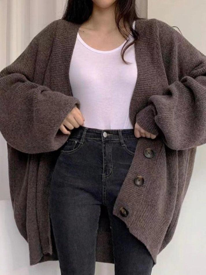 Femme portant un cardigan oversize en maille marron avec de grands boutons sur le devant. Le vêtement est associé à un t-shirt blanc ajusté et un jean taille haute noir, créant un look décontracté, élégant et parfait pour les journées fraîches.