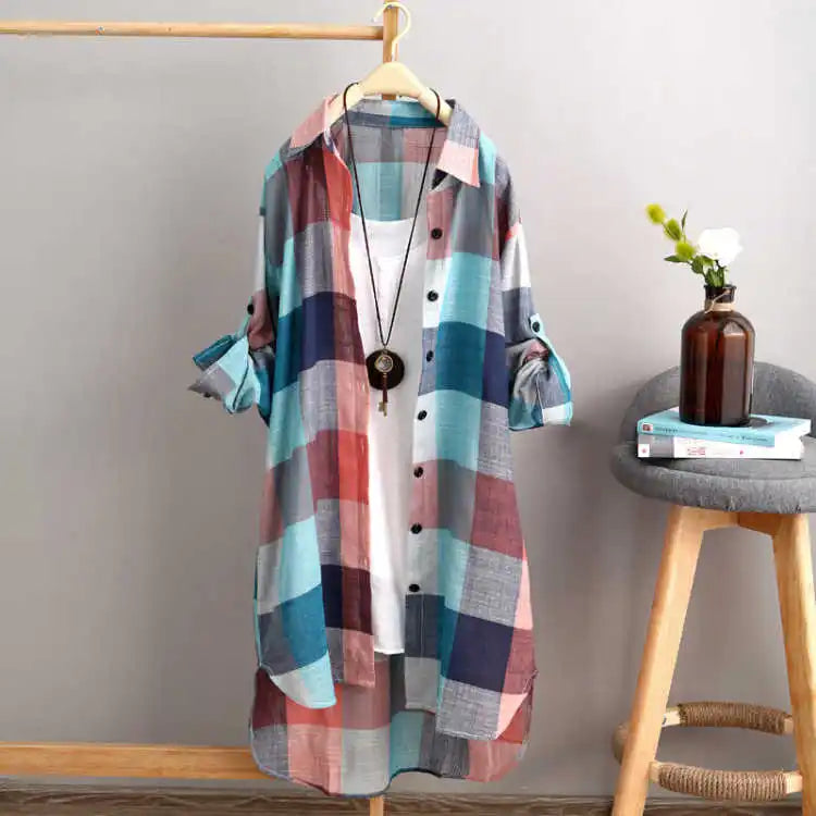Chemise boutonnée femme Perrine moderne à carreaux multicolores (bleu, rouge et gris), coupe longue avec manches retroussées, présentée sur cintre dans un intérieur déco.