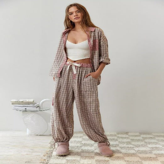 Pyjama pour femme à carreaux avec un haut à manches longues et un pantalon confortable à taille élastiquée. Le look est complété par des poches pratiques et des baskets roses, offrant un style moderne et décontracté, idéal pour une tenue de nuit stylée.